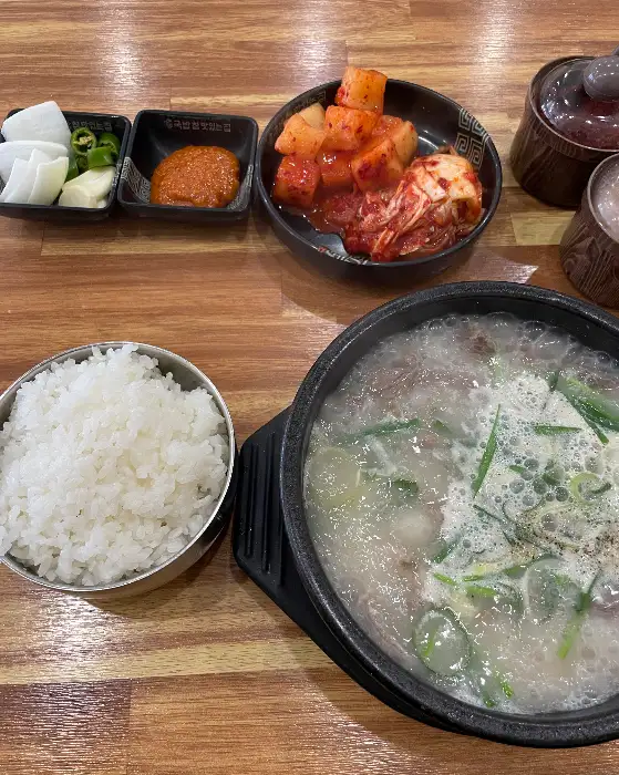 김치, 깍두기, 다진 마늘, 새우젓이 담긴 반찬 접시와 국밥, 밥
