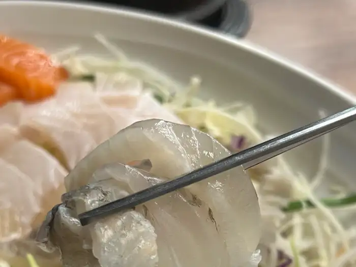 젓가락으로 집은 또 다른 흰 살 생선회 조각. 더욱 촘촘한 근육결이 보이는 듯하다.