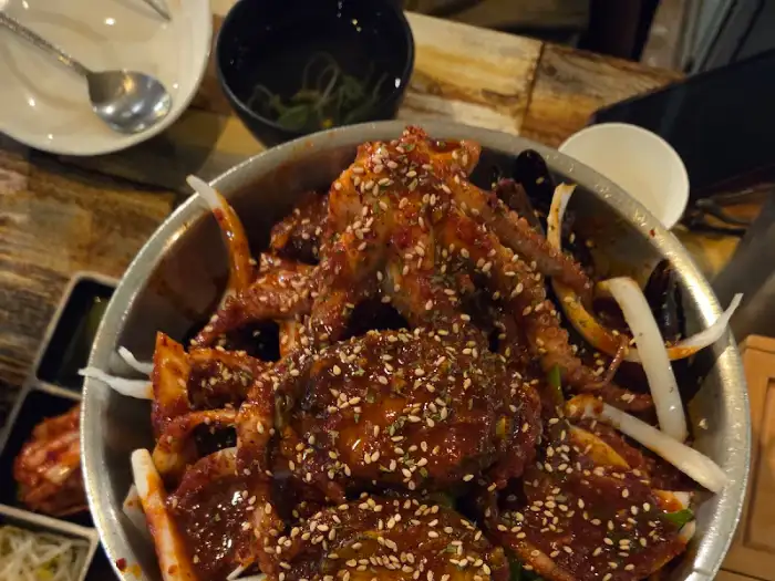 메인 찜 요리는 다양한 해산물과 고기, 그리고 붉은 양념이 어우러져 한 폭의 그림 같은 비주얼을 자랑한다. 큼지막한 낙지와 소갈비, 전복 등이 푸짐하게 담겨 있다.