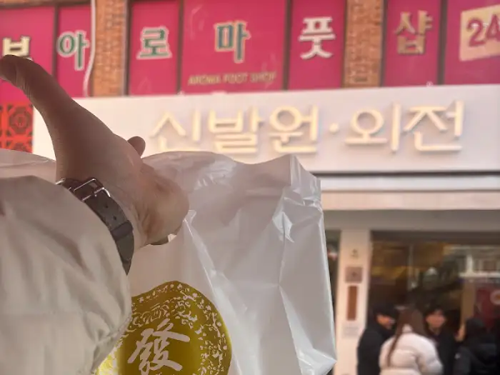 신발원 간판이 보이는 거리 풍경, 손이 하얀 봉투를 들고 있다.