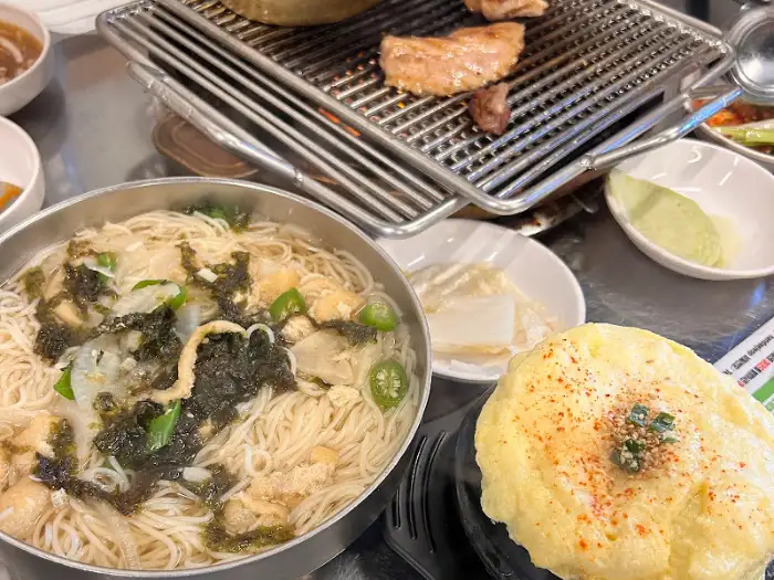 식탁 위에 놓인 국수와 계란찜, 그리고 불판 위 고기가 보입니다.