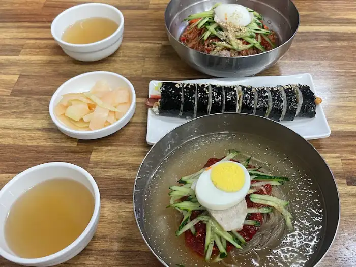 테이블 위에 놓인 음식들의 전체적인 모습입니다. 금속 쟁반에 담긴 물밀면과 비빔밀면, 김밥 한 줄, 그리고 작은 종지에 담긴 단무지와 온육수가 보입니다.