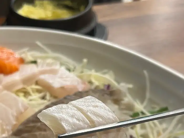 젓가락으로 집어 올린 신선한 흰 살 생선회 조각