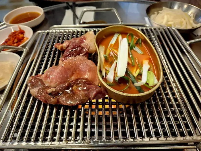 지글거리는 불판 위에서 익고 있는 고기와 된장찌개가 보입니다.