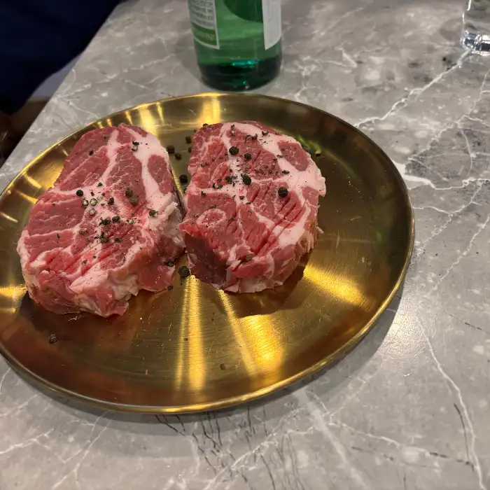 금빛 도금 접시에 신선한 꽃목살 덩어리가 놓여 있는 모습