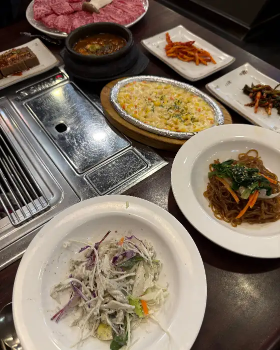 숯불 위에서 구워지고 있는 소고기, 주변에는 다양한 반찬과 찌개가 보인다