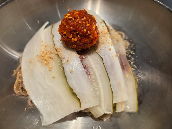 메밀면 위에 얇게 썬 오이와 매콤한 양념이 얹어진 비빔국수.