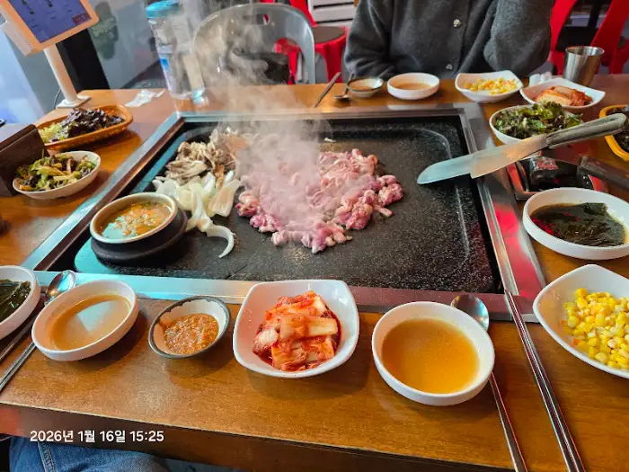 돌판 위에서 오리 요리가 익어가고, 주변에 곁들임 반찬들이 놓인 모습