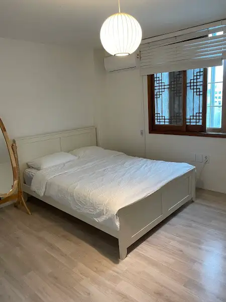 흰색 침대가 놓인 침실. 창문에는 격자무늬가 있고, 조명이 켜져 있다.