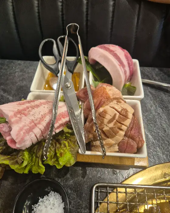 신선한 생고기 덩어리와 양념된 고기 덩어리, 그리고 가위와 집게가 놓여있는 모습