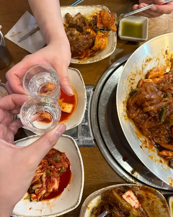 두 개의 소주잔에 소주가 담겨 있고, 앞쪽으로는 김치와 뼈찜 조각이 놓여 있습니다.