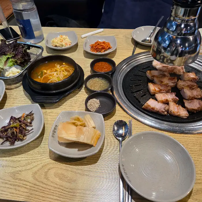 고기와 다양한 밑반찬, 쌈 채소, 찌개가 함께 차려진 식탁 모습