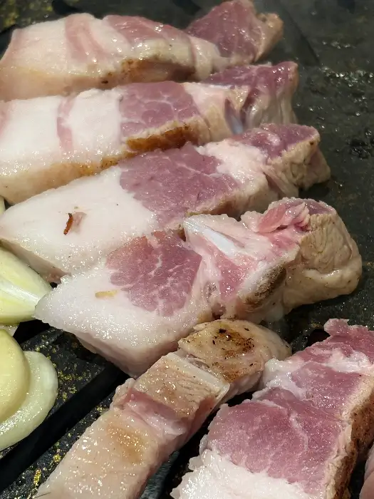 두툼하게 썰린 흑돼지 삼겹살 조각들이 불판 위에서 익어가고 있다