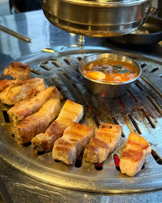 두툼한 흑돼지 목살과 오겹살이 불판 위에서 지글지글 익어가고 있고, 작은 뚝배기에는 멜젓이 담겨 있다