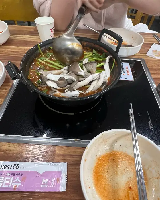 칼국수 냄비에 담긴 버섯과 미나리, 그리고 국자를 이용해 국물을 뜨는 모습