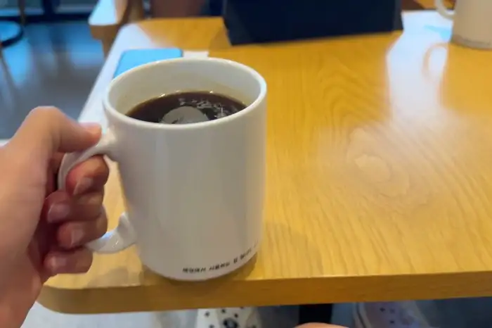 한 손으로 들고 있는 흰색 머그컵에 담긴 커피