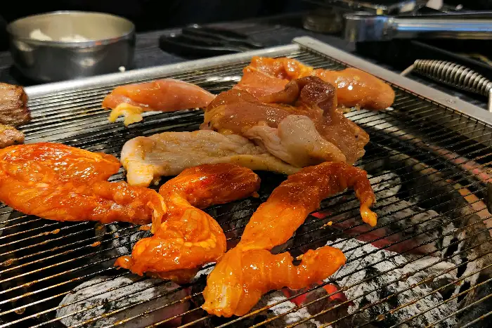 양념된 닭고기와 돼지고기가 숯불 위에서 익고 있는 모습