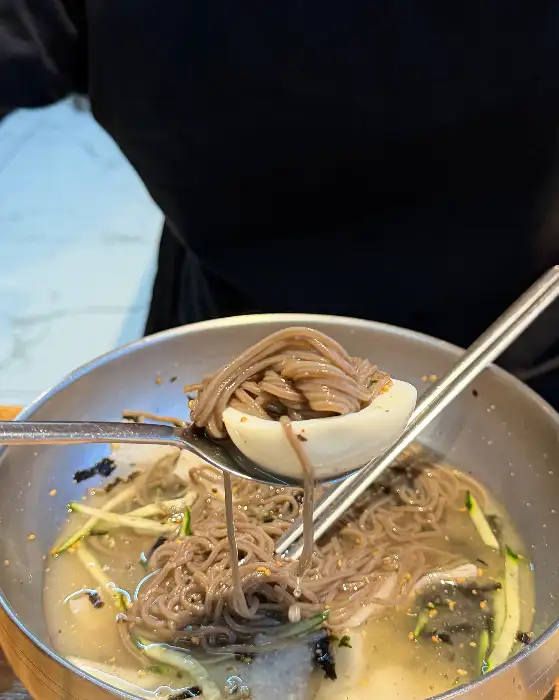 메밀국수가 담긴 그릇과 숟가락에 얹어진 삶은 달걀 단면