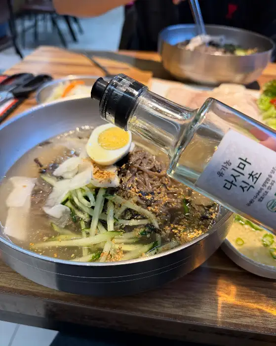 다시마 식초병이 막국수 그릇 위에서 기울어져 있는 모습