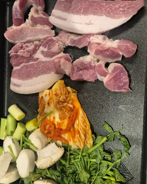 불판 위에서 익어가는 삼겹살 조각들과 잘 익은 김치