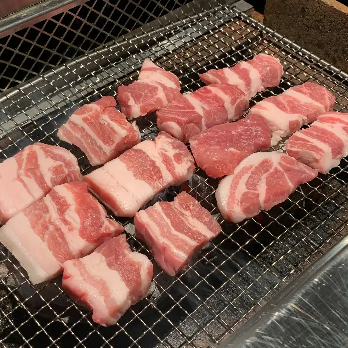 다양한 두께로 썰린 고기들이 숯불 석쇠 위에 놓여 익어가고 있는 모습