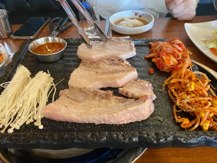 불판 위에 올려진 두툼한 고기와 곁들임 재료들