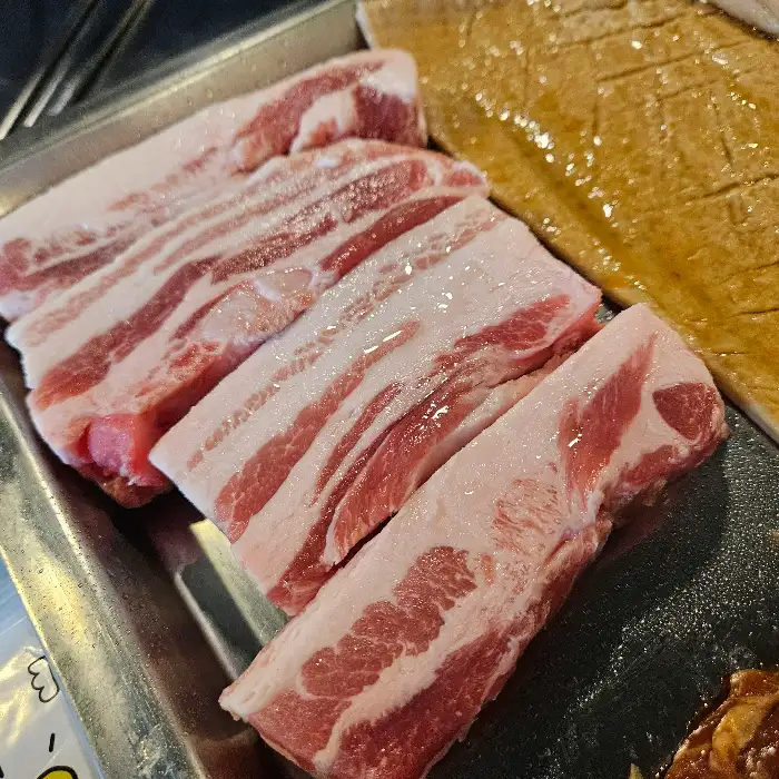 신선한 삼겹살이 먹음직스럽게 줄지어 접시에 담겨 있다. 붉은 살코기와 하얀 비계의 대비가 선명하다.