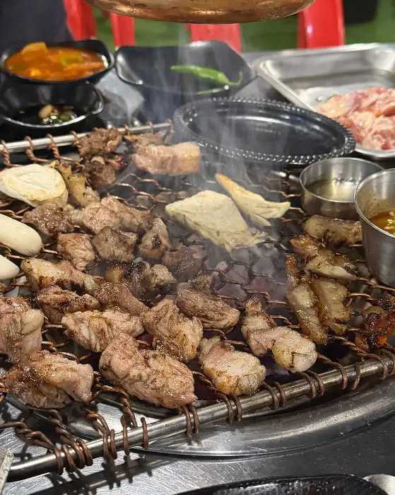 다양한 종류의 고기가 숯불 위에서 굽히고 있으며, 훈연 향이 피어오른다.