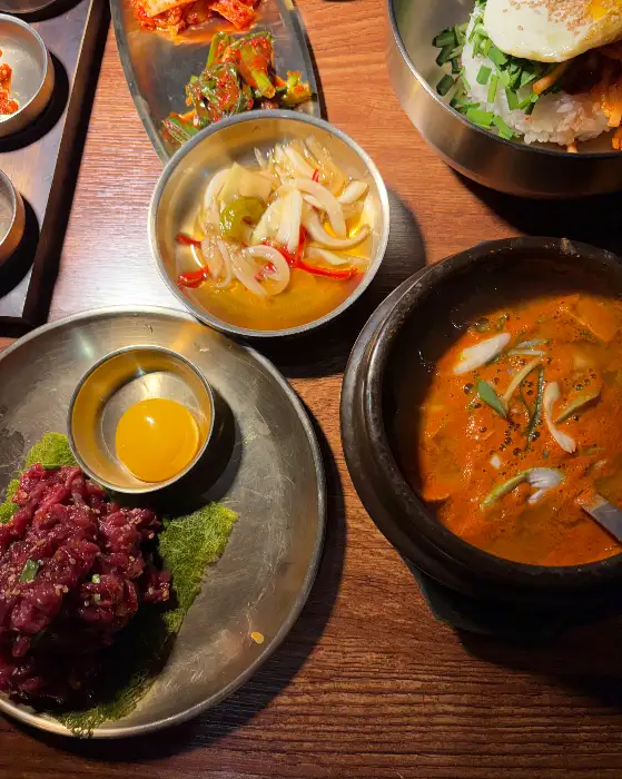 테이블 위에 차려진 다양한 반찬들과 함께 육회, 비빔밥, 그리고 찌개까지 보인다.