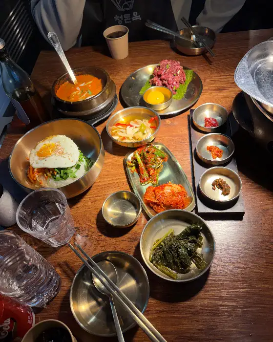 테이블 위에 다양한 음식들이 차려져 있는 모습. 육회, 찌개, 비빔밥 등이 보인다.