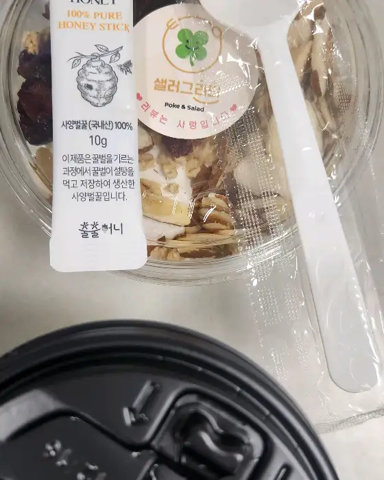 작은 꿀 스틱과 샐러그리티 로고가 보이는 포케 용기