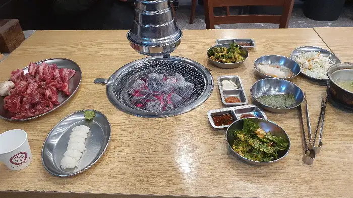 테이블 세팅 전체 모습. 숯불, 고기, 밑반찬 등이 준비되어 있음