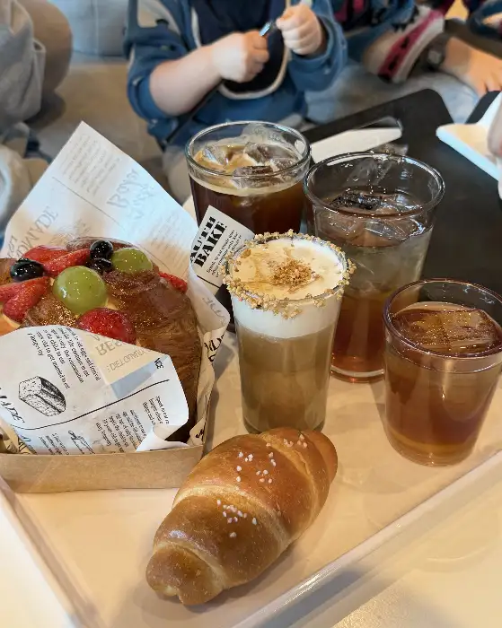 쟁반 위에 크루아상, 빵 조각, 그리고 여러 잔의 음료가 놓여 있다. 빵은 먹음직스럽게 구워져 있으며, 음료는 크림이나 얼음이 들어 있다.