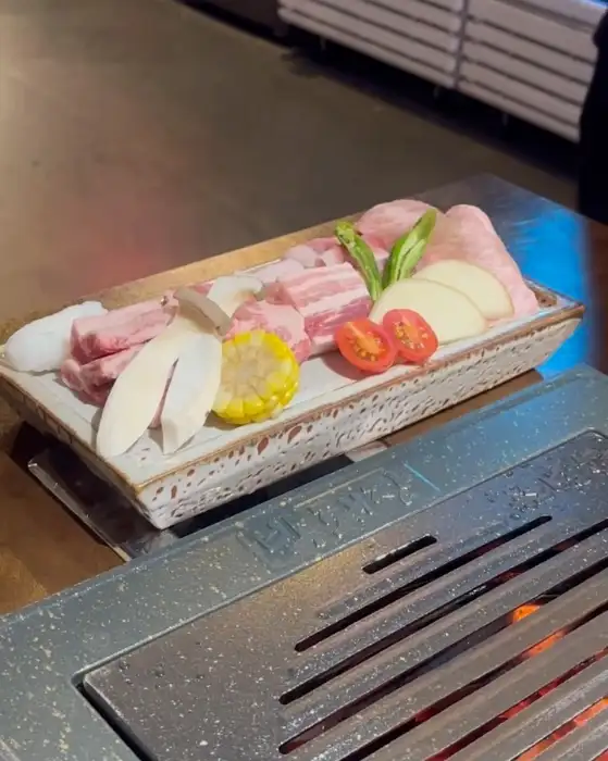 불판 위에 가지런히 올려진 신선한 고기 모듬, 버섯, 옥수수, 토마토