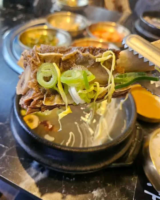 갈비탕 국물에 담긴 큼직한 갈비 살점. 젓가락으로 집어 올렸을 때 부드럽게 분리되는 모습이 보입니다.