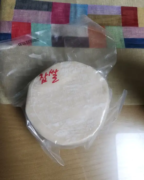 투명한 비닐 포장 안에 둥글납작한 떡볶이 떡이 들어 있습니다. 떡의 겉면에는 하얀 밀가루가 살짝 묻어 있고, 붉은색 글씨로 '쫄깃'이라고 쓰여 있습니다.