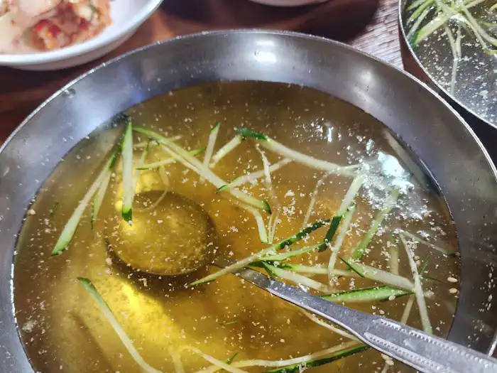 투명하고 맑은 육수 안에 얇게 썬 오이가 띄워진 물냉면 육수의 모습.