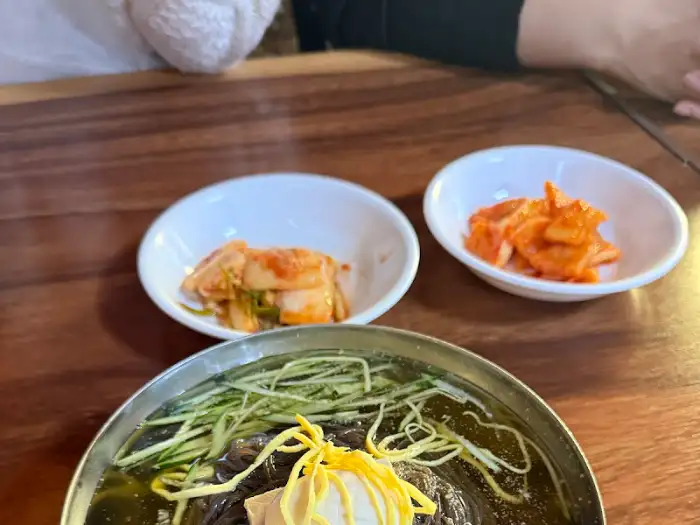 작은 그릇에 담긴 김치와 물냉면 또는 비빔냉면이 함께 놓인 테이블 풍경.