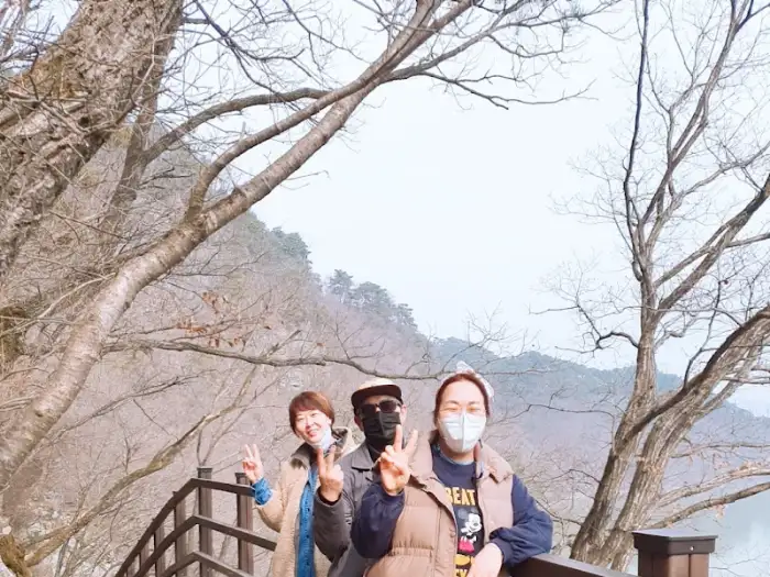 세 명의 사람들이 다정한 모습으로 카메라를 향해 웃고 있다. 계절감을 느끼게 하는 따뜻한 옷차림과 밝은 표정이 행복한 순간을 담고 있다.