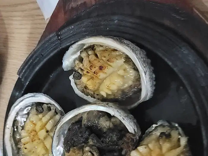 먹음직스럽게 구워진 전복이 조개껍질 위에 올려져 있는 모습