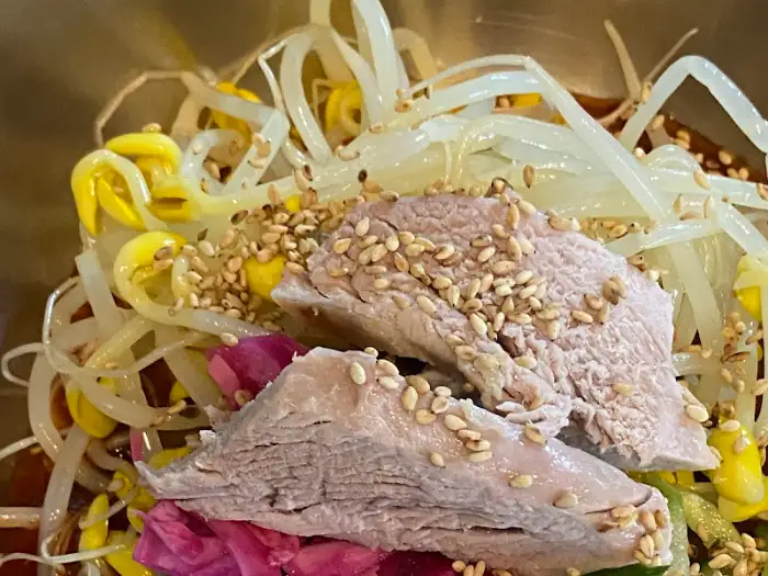 비빔국수 위에 올라간 얇게 썬 고기와 콩나물, 깨