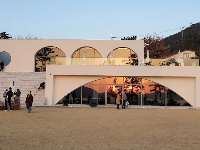흰색 건물의 독특한 아치형 디자인, 넓은 잔디밭과 계단이 보인다.