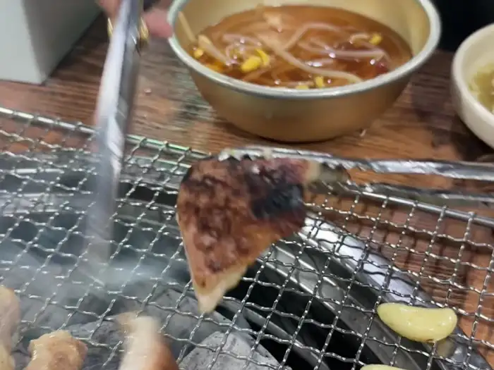 집게로 갈매기살 한 점을 집어 굽는 모습