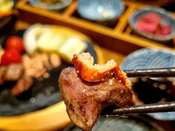 집게로 양갈비 한 점을 집어 올린 모습. 갈비 위에 빵 조각 같은 것이 얹혀 있다.