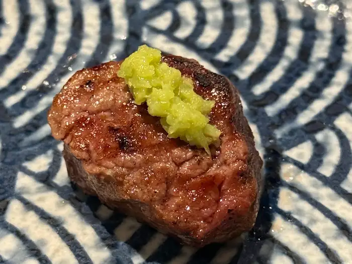 동그란 양갈비 조각 위에 연두색 소스가 얹혀 있는 모습. 접시는 파란색과 흰색의 물결 무늬가 특징이다.