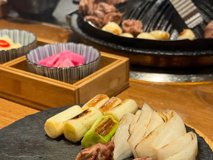 구워진 파와 토마토, 그리고 양파가 접시에 담겨 있다. 뒤로는 숯불 불판과 반찬 그릇들이 보인다.