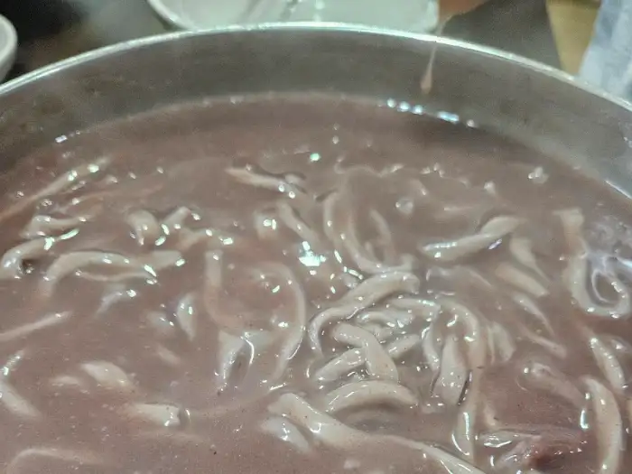 붉은빛이 도는 팥칼국수 국물 속에 얇고 부드러운 면발이 얽혀 있다.