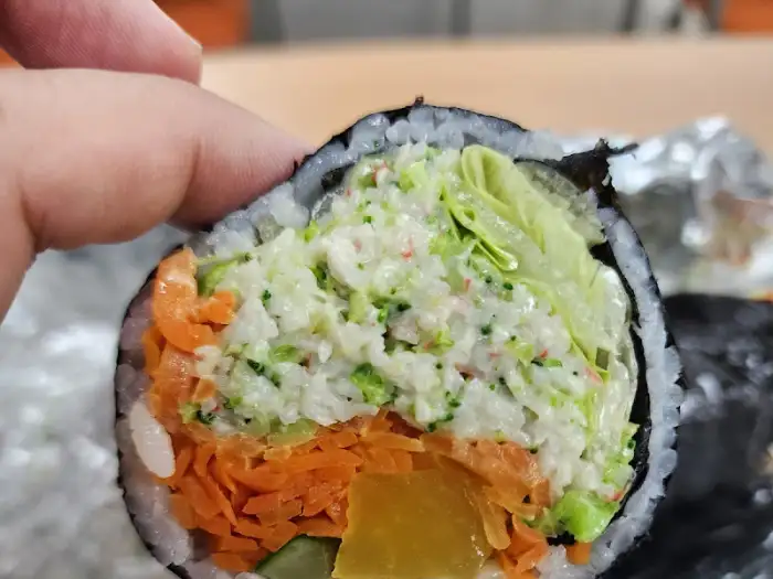 손으로 샐러드 김밥 한 조각을 들고 있는 모습