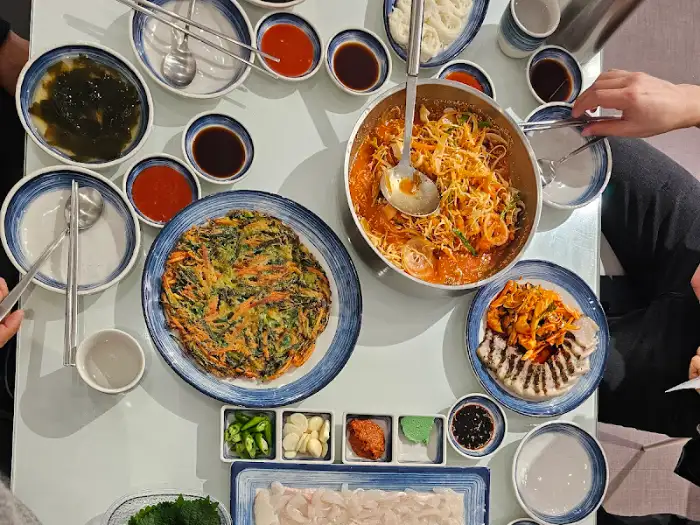 테이블 위에 차려진 다양한 음식 사진: 파전, 매운탕, 곁들임찬, 밥, 술잔 등
