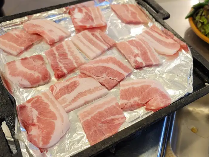 불판 위에서 맛있게 익어가고 있는 냉동 삼겹살의 클로즈업 사진
